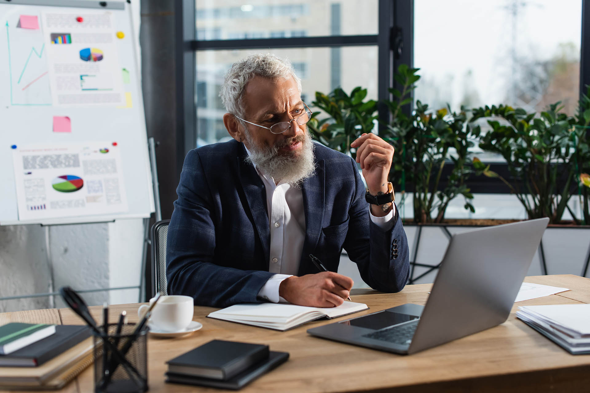 Middle aged businessman in eyeglasses writing on notebook and us