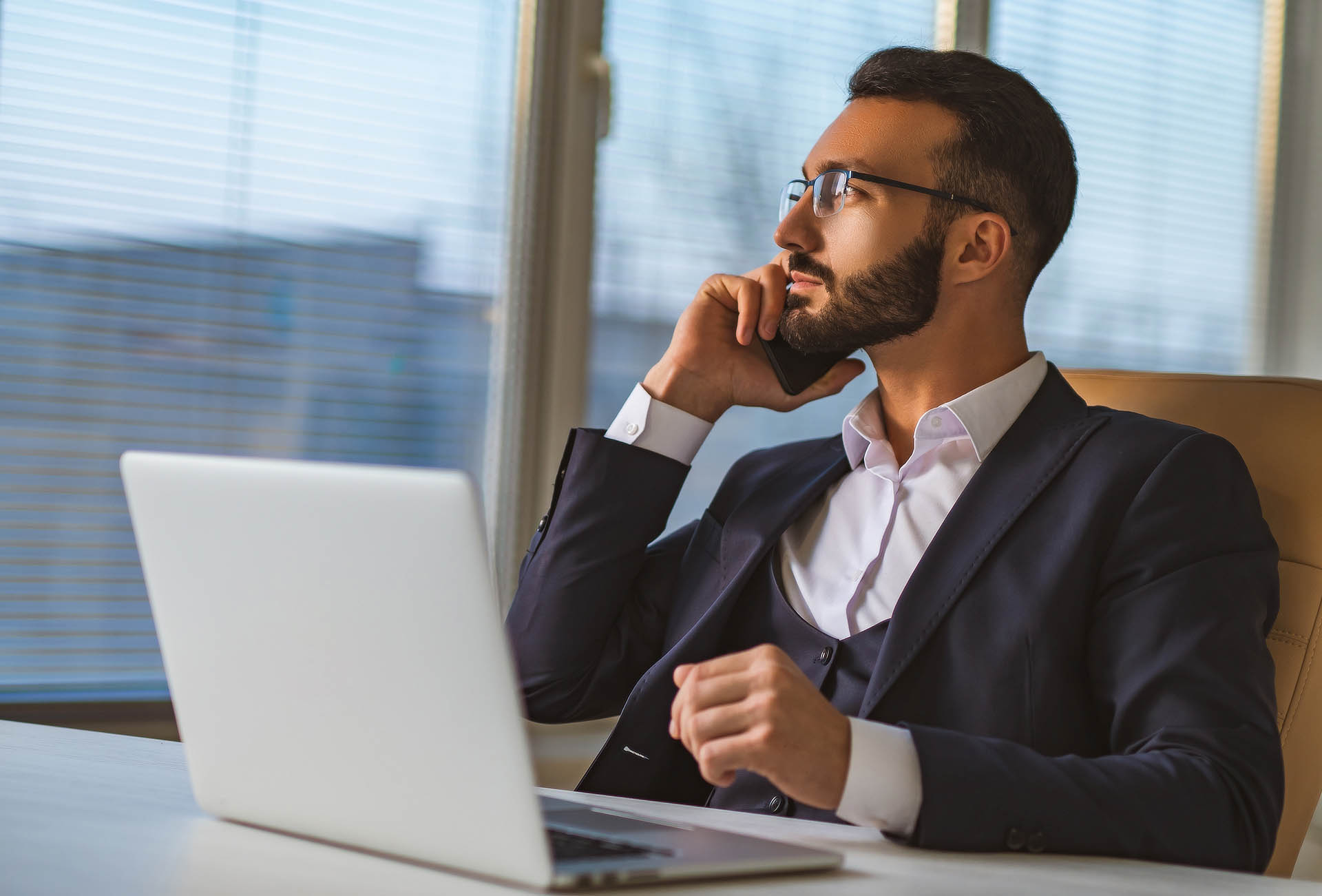 The businessman in glasses sitting at the desk and phoning